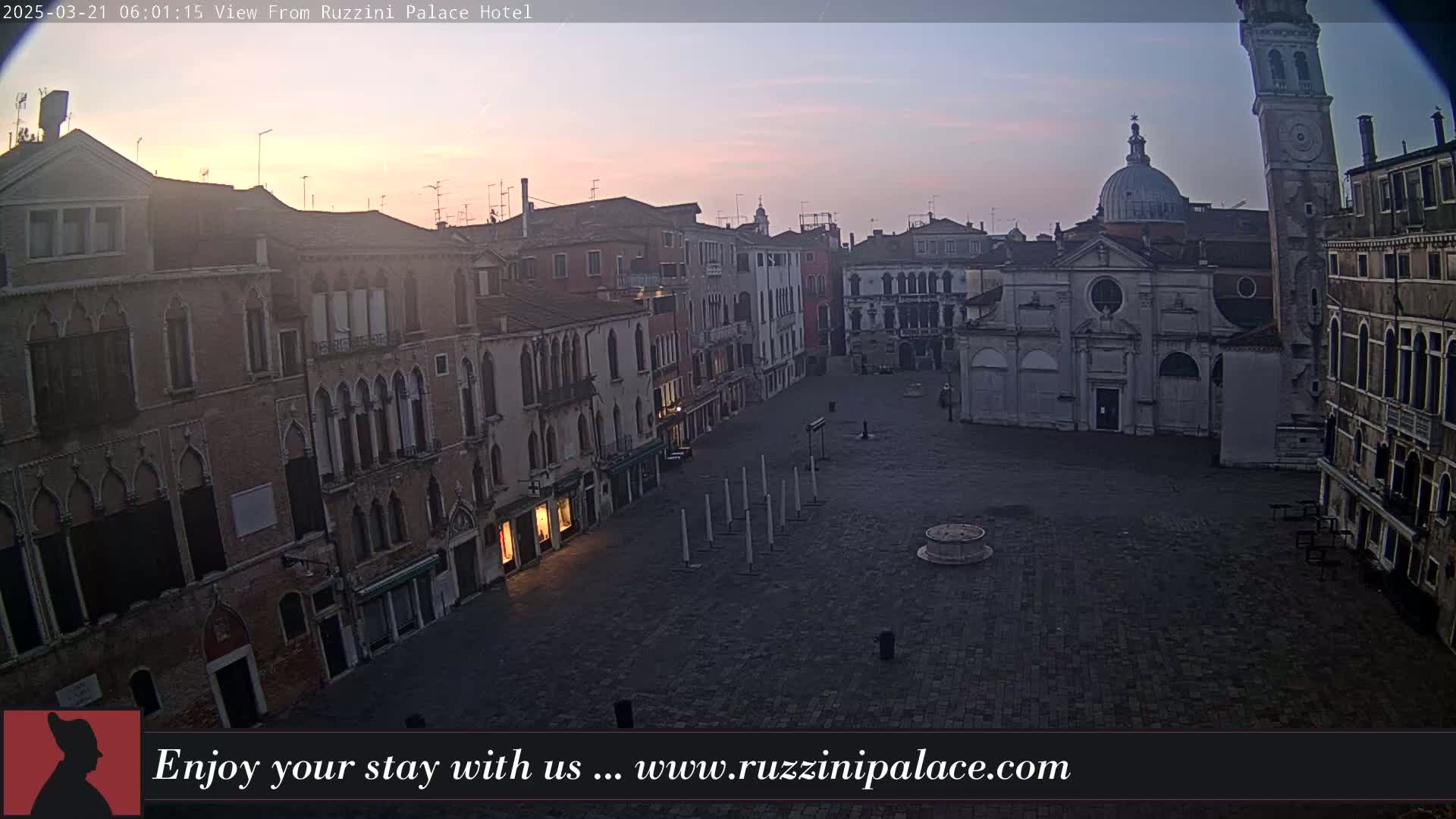 A mostly empty, brick plaza in a city is seen at sunrise, with several old buildings surrounding it.