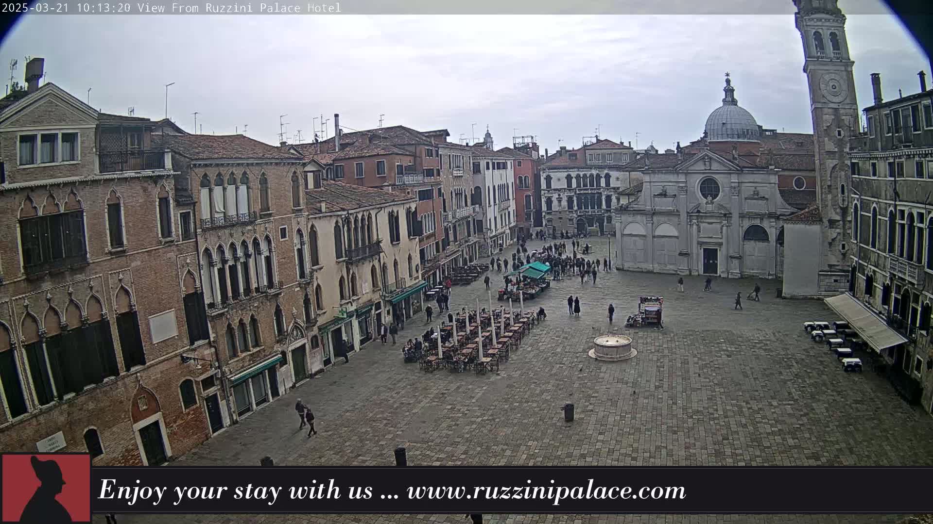 A mostly empty cobblestone square in Venice, Italy, is surrounded by historic buildings under an overcast sky.