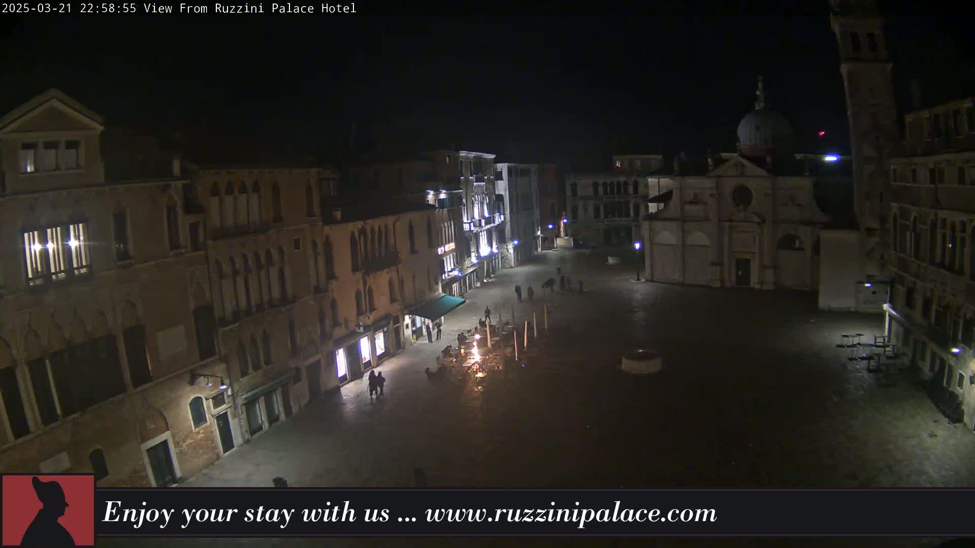 A nighttime, high-angle view of a dimly lit, cobblestone square in Venice, surrounded by historic buildings.