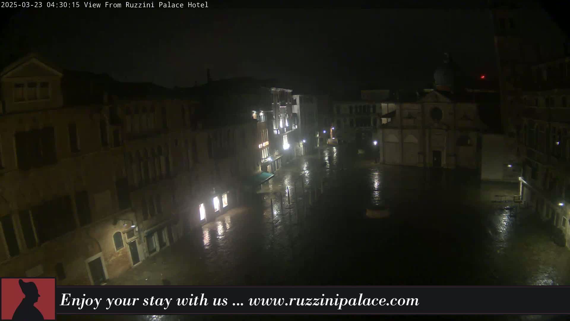 A nighttime view of a rain-soaked Venetian square, surrounded by buildings, with dim lighting reflecting on the wet pavement.