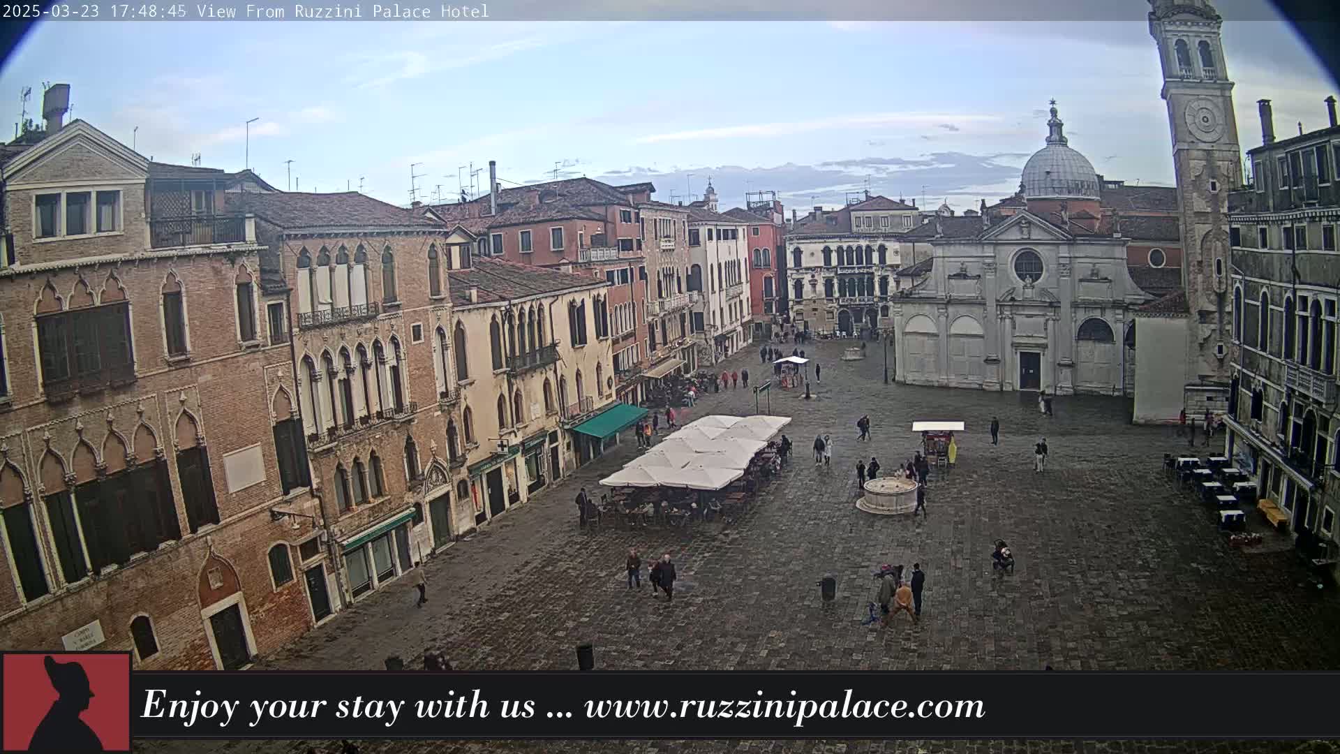 A large, mostly empty cobblestone square in a city is surrounded by tall, old buildings under a partly cloudy sky.