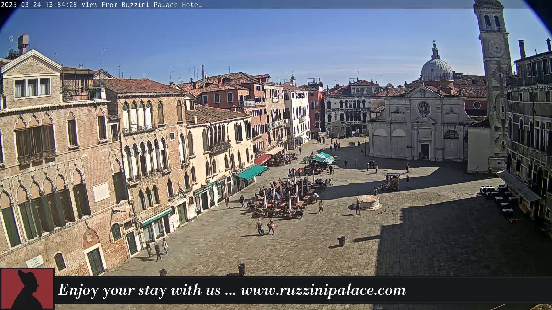 A sunny day reveals a large, mostly empty plaza in Venice, Italy, surrounded by historic buildings, with a few people scattered about and outdoor seating areas.