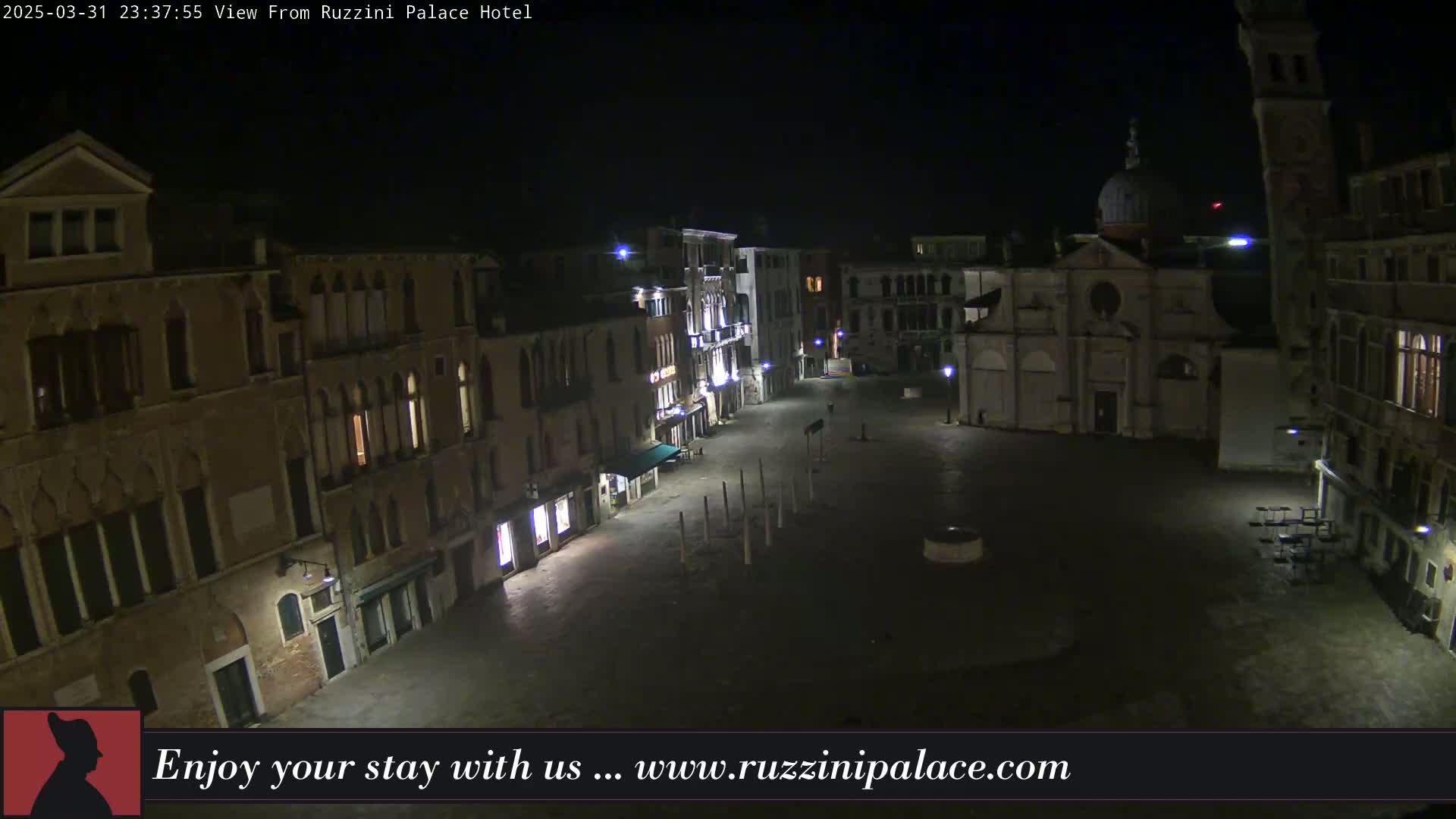 A nighttime view of a mostly empty, paved plaza in Venice, Italy, surrounded by old buildings.