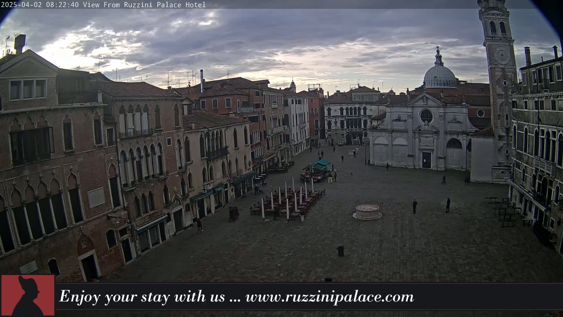 A mostly empty, large cobblestone square in Venice, Italy is surrounded by old brick buildings under an overcast sky.