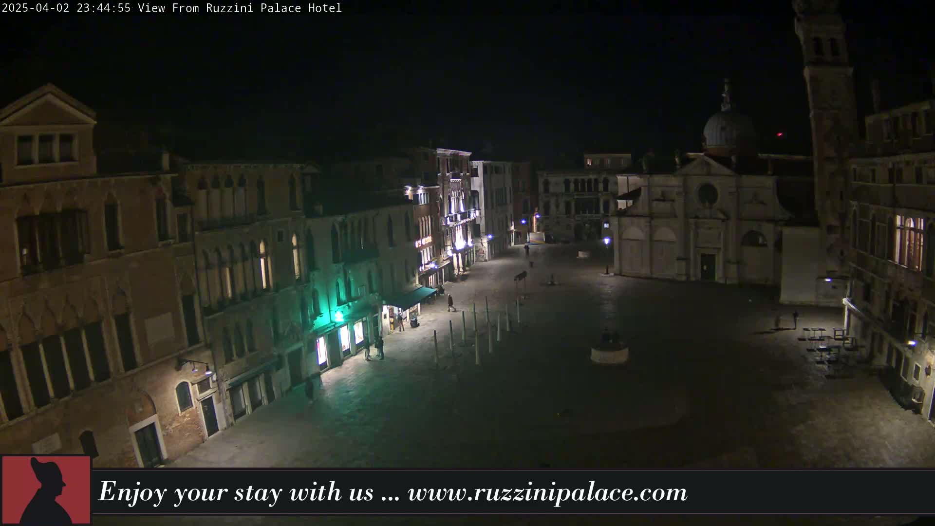 A nighttime view of a sparsely populated plaza in Venice, Italy, surrounded by old buildings under a clear, dark sky.