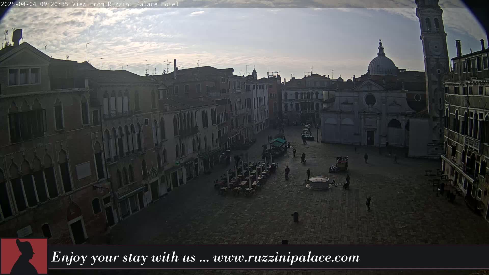 A mostly empty cobblestone square in Venice, Italy, is surrounded by aged buildings under a partly cloudy sky.
