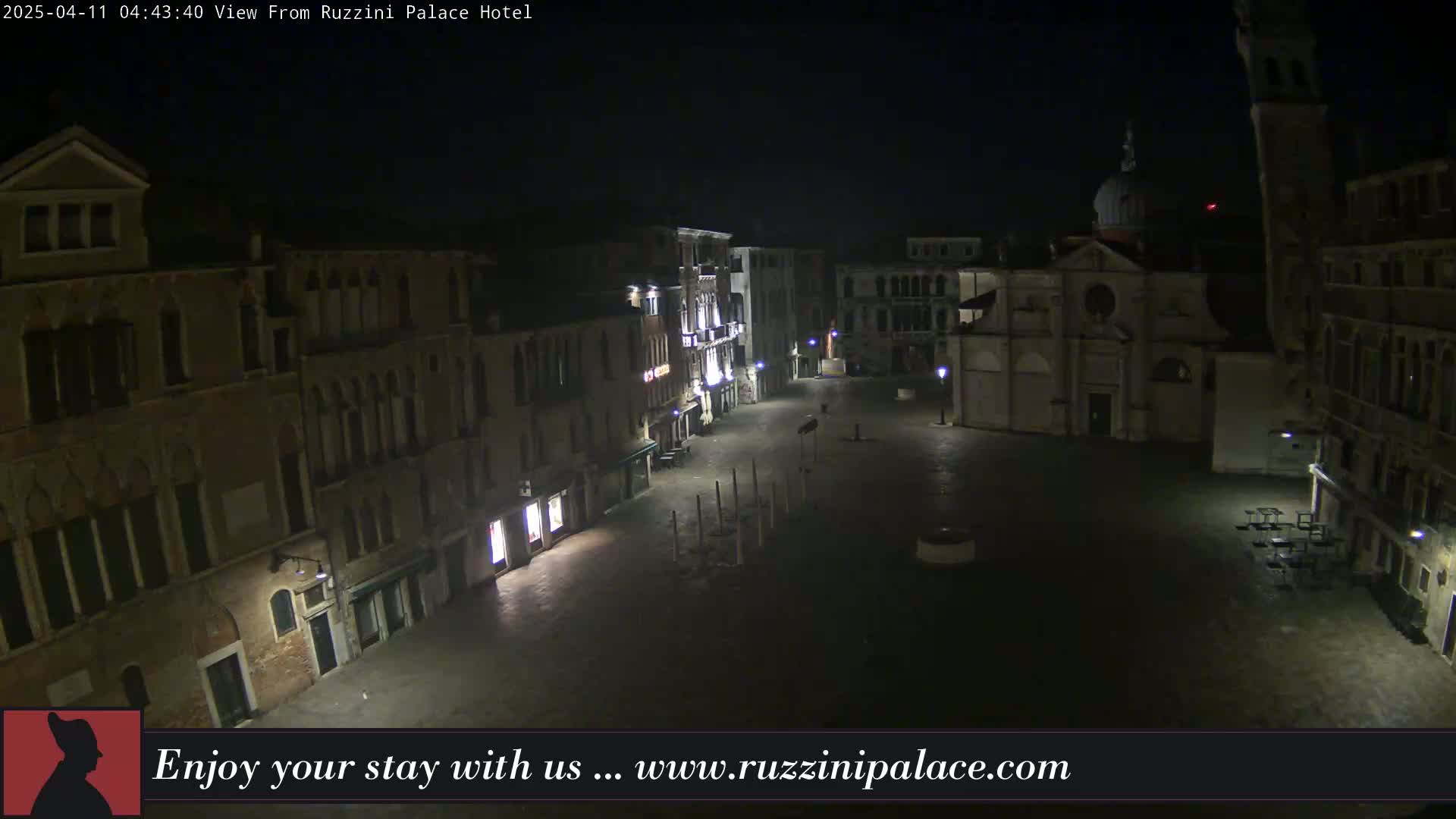 A nighttime view of a deserted, stone plaza in Venice, Italy, surrounded by old buildings.