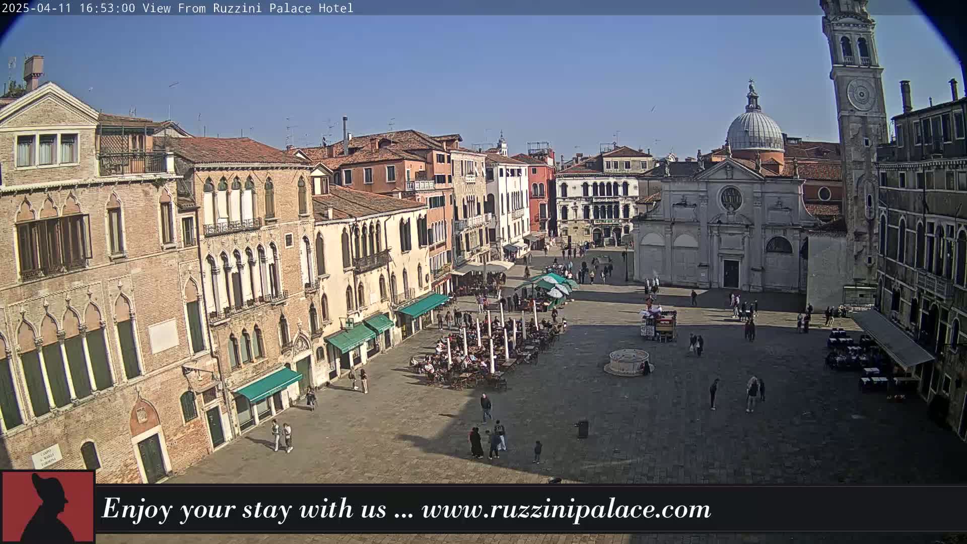 A sunny day in a large, paved European square surrounded by historic buildings, with people sitting at outdoor cafes.