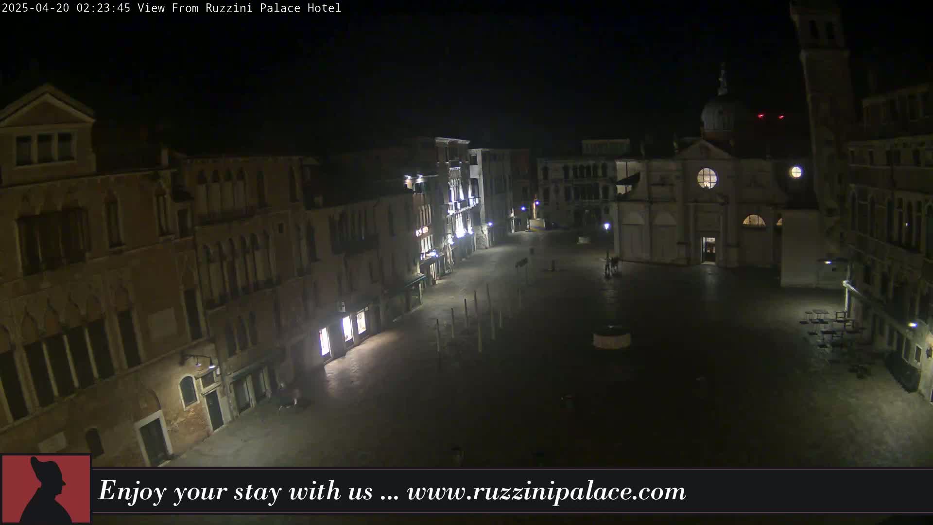 A nighttime view of a deserted, cobblestone square in Venice, Italy, surrounded by old buildings, with a church in the background.