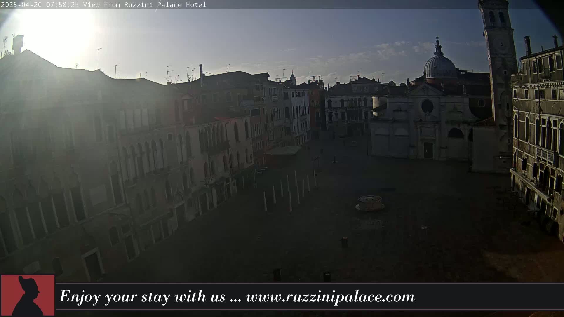 A mostly empty, sunlit Venetian square is surrounded by old buildings under a mostly clear sky.
