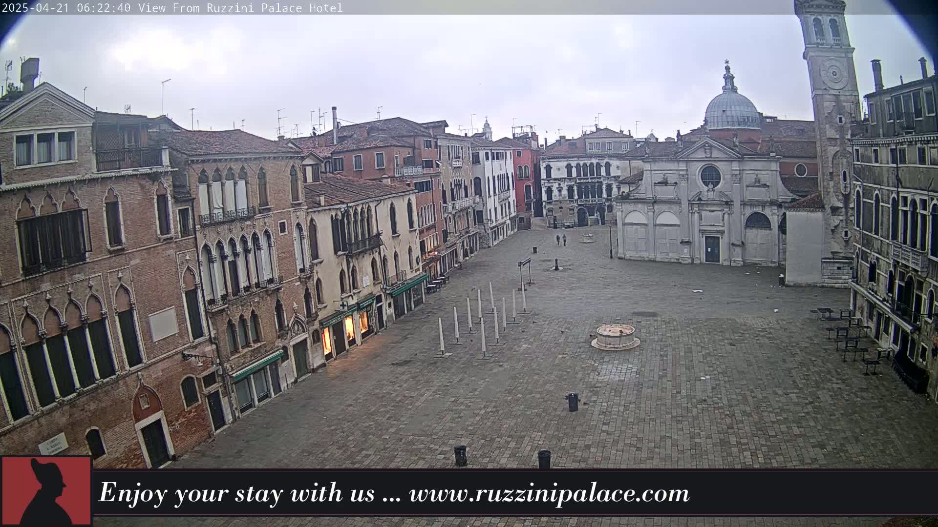 A mostly empty cobblestone square in Venice, Italy, is surrounded by aged brick buildings under an overcast sky.