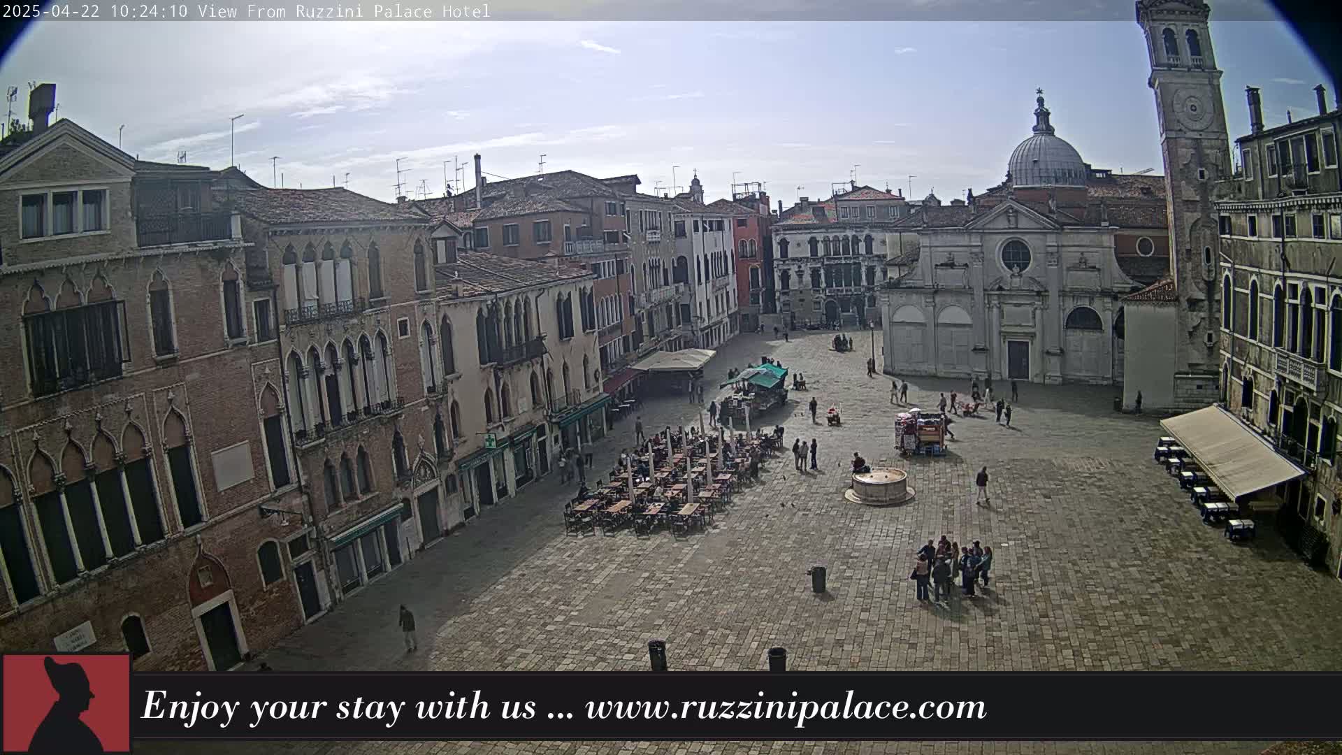 A large, paved square in a European city is surrounded by several-story brick buildings, under a partly cloudy sky.