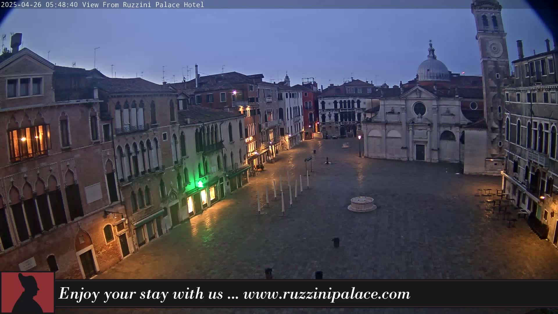 A mostly empty, cobblestone plaza in Venice, Italy, is dimly lit at dawn under a twilight sky.