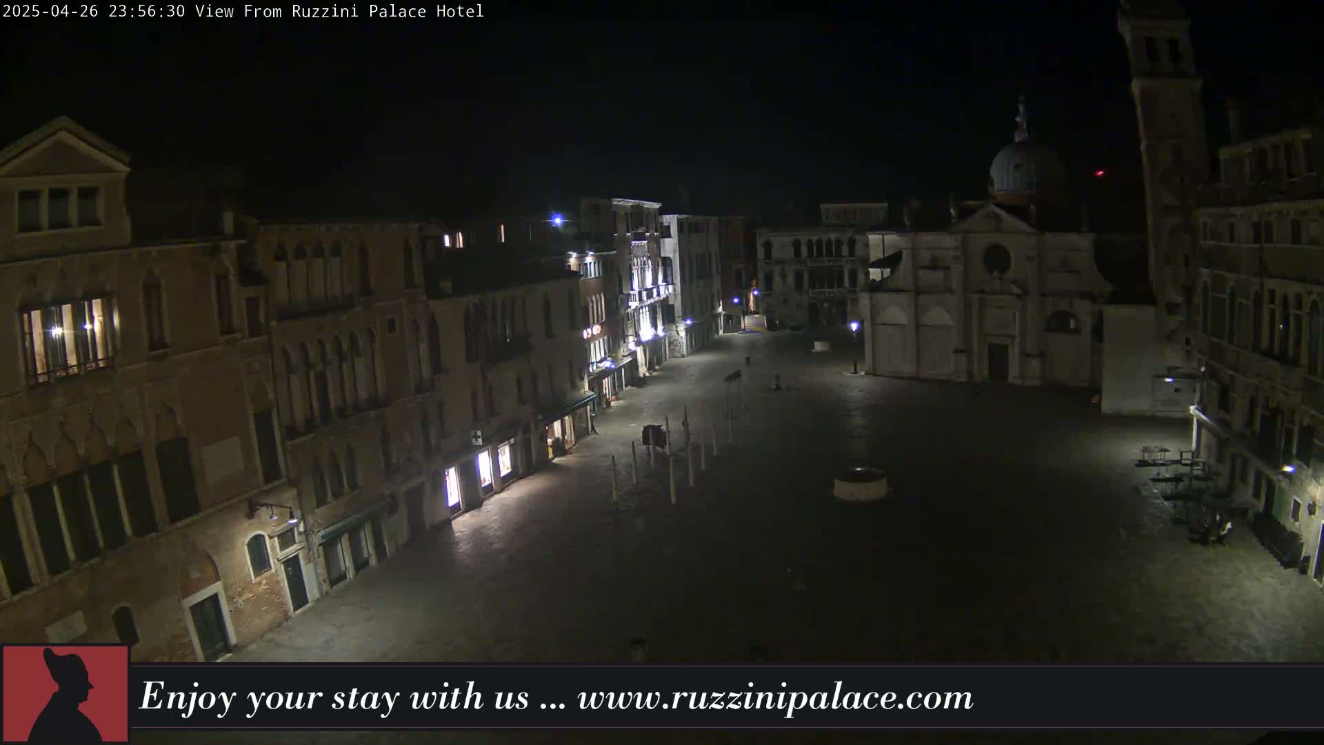 A nighttime view of a dimly lit, empty plaza in a European city, surrounded by old buildings.