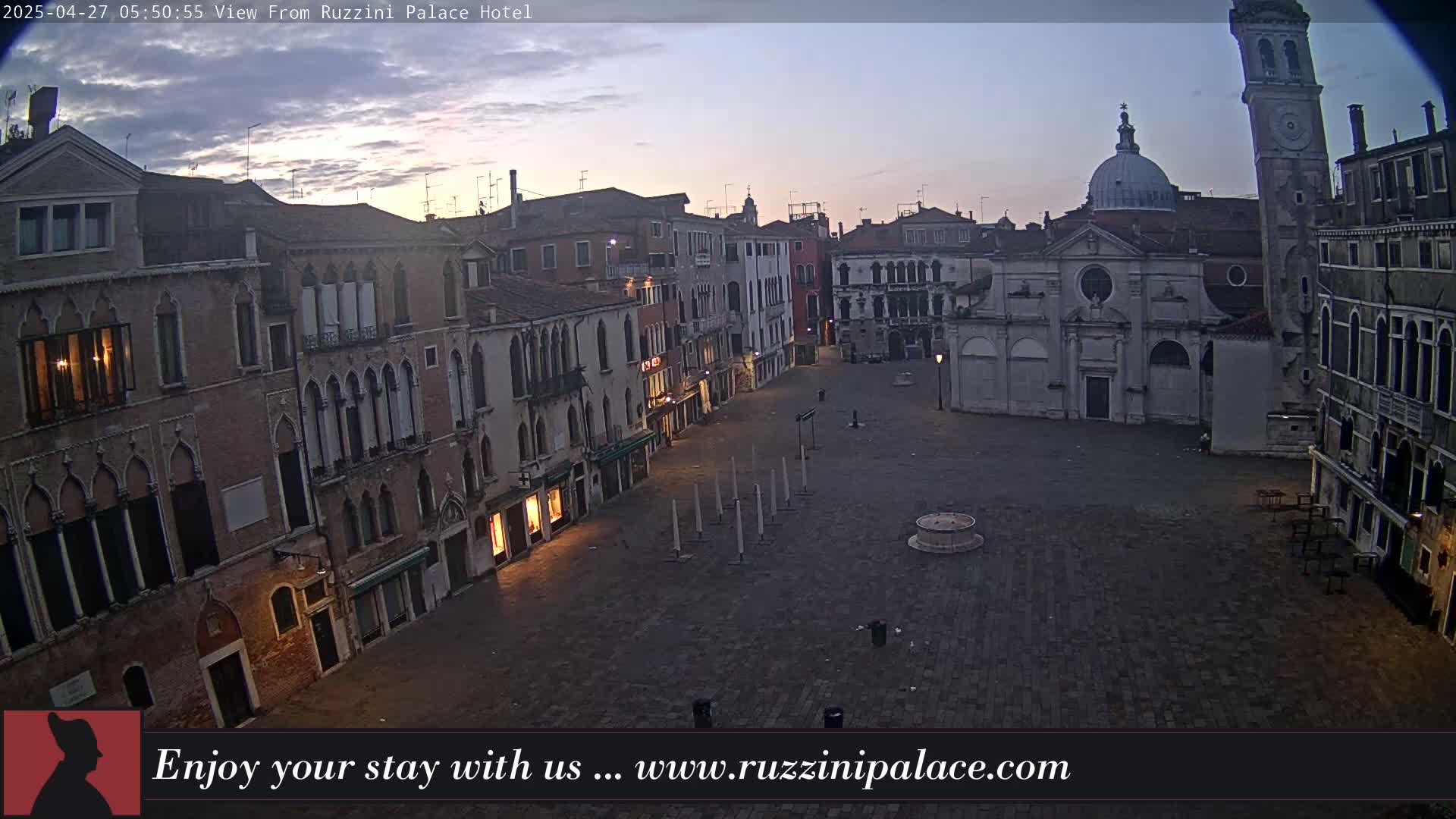 A mostly empty, cobblestone square in Venice, Italy, is surrounded by old brick buildings under a twilight sky.