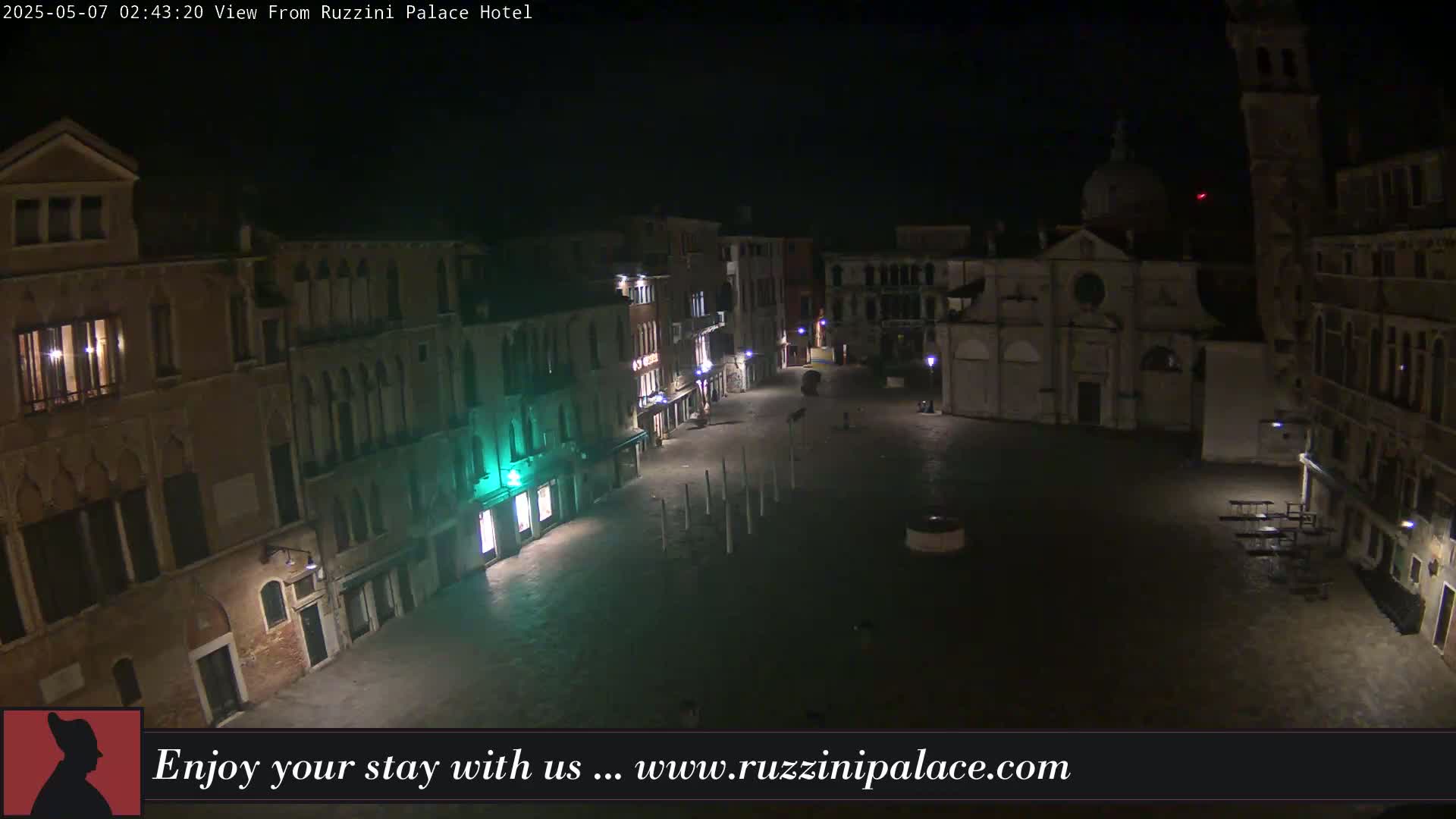A nighttime view of a deserted, cobblestone square in Venice, Italy, surrounded by old buildings, is illuminated by streetlights.