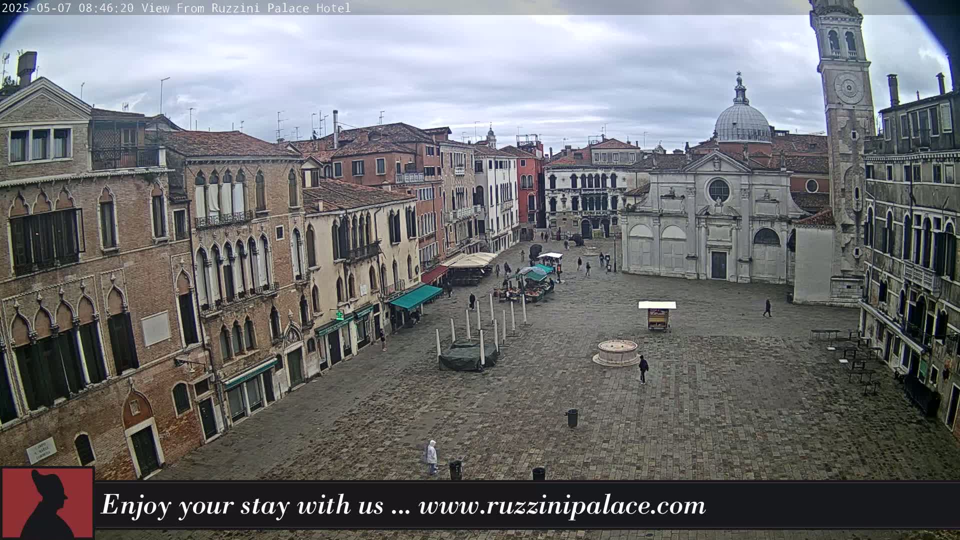 A large, mostly empty cobblestone square in a city is surrounded by several-story buildings under an overcast sky.