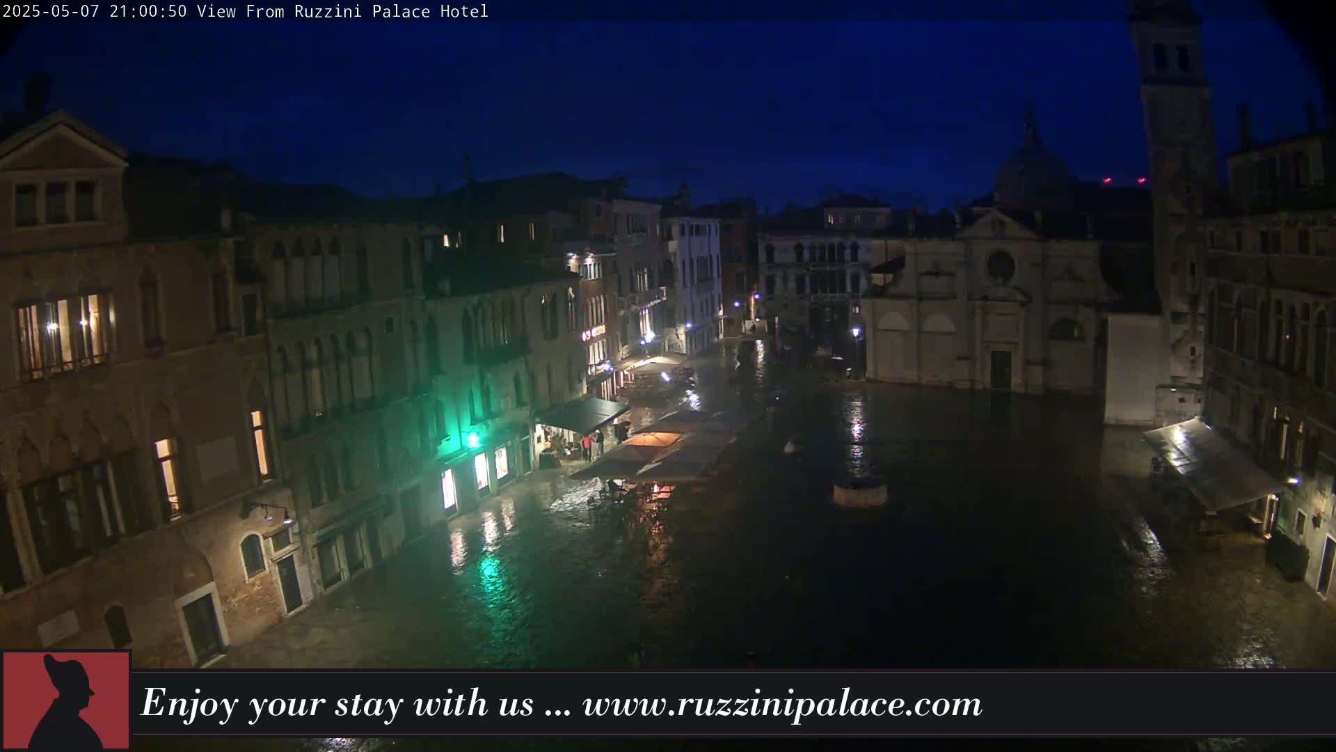 A nighttime view of a flooded Venetian square, surrounded by old buildings under a dark blue sky.