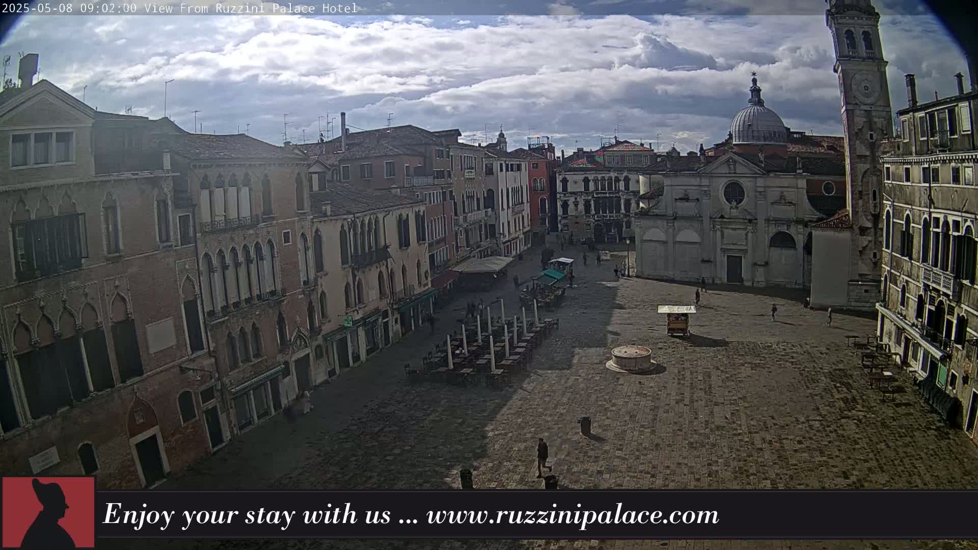 A mostly cloudy sky hangs over a large, empty plaza in Venice, Italy, surrounded by ancient buildings.