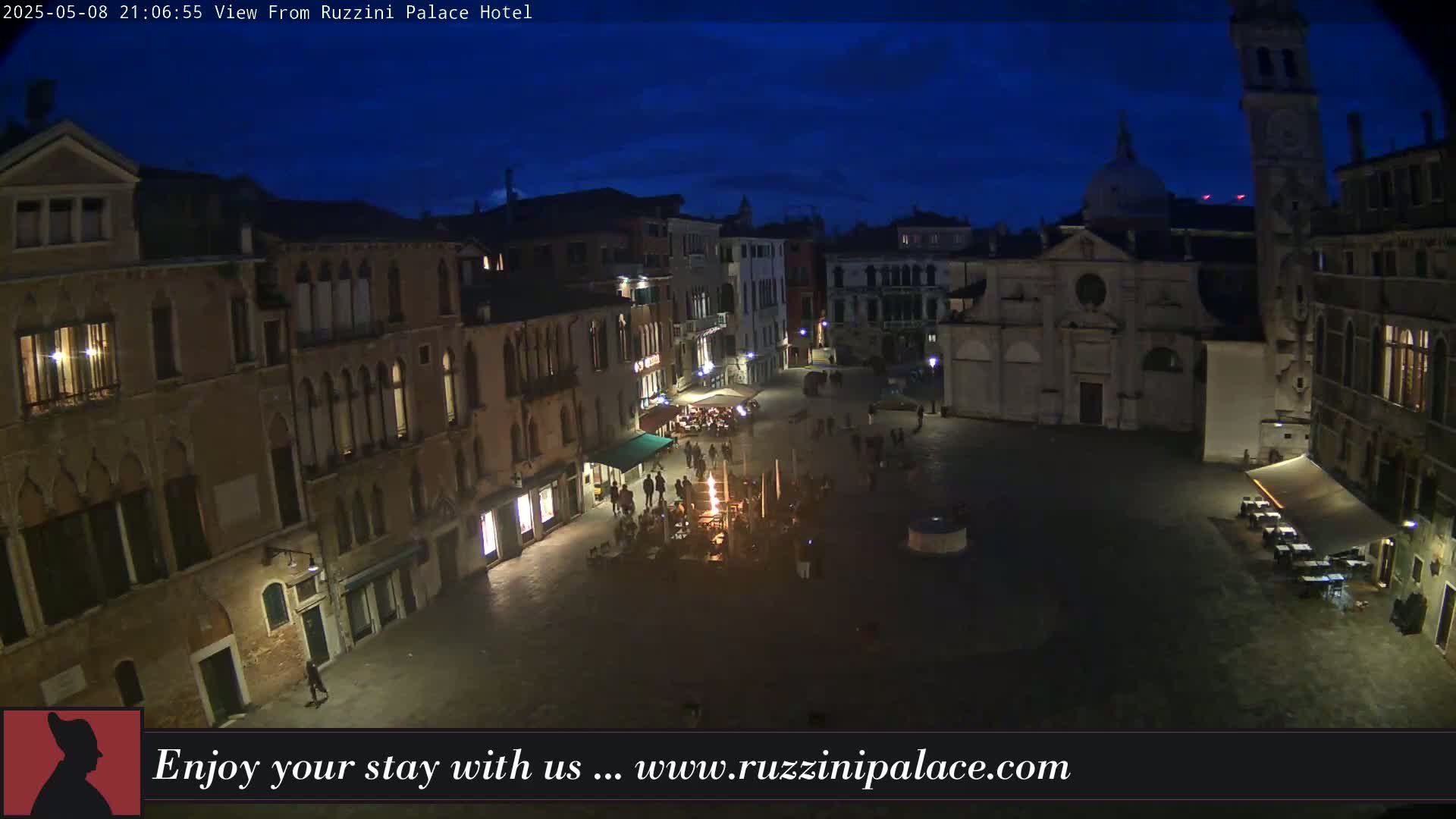 A nighttime view of a dimly lit European-style square surrounded by old buildings under a dark blue sky.