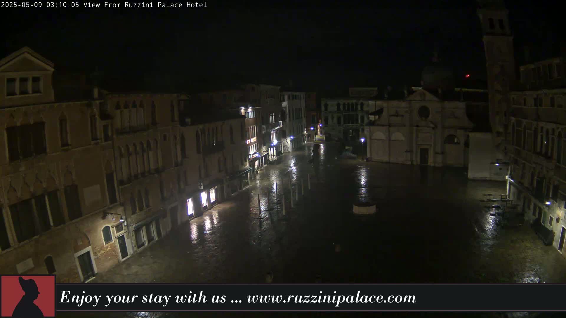 A nighttime view of a rain-soaked square in Venice, surrounded by old buildings.