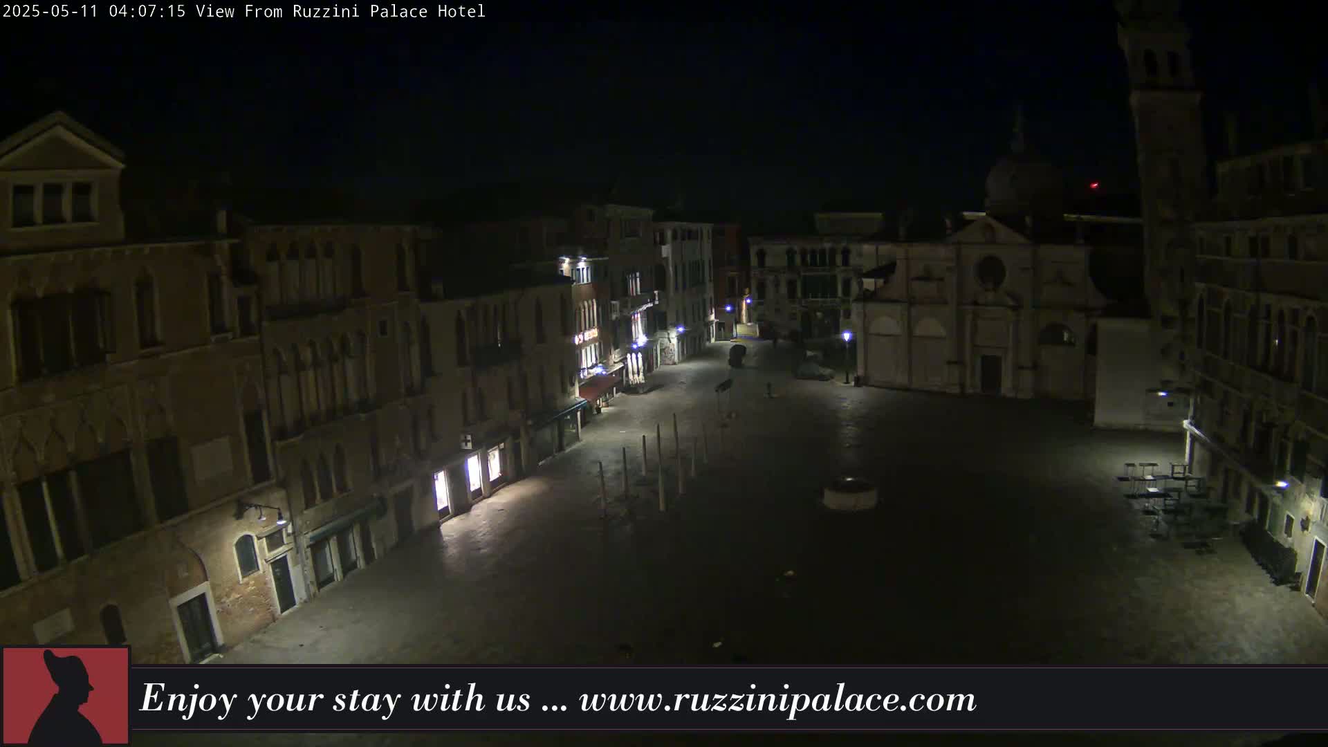 A nighttime view of a dimly lit, empty European-style square surrounded by old buildings.