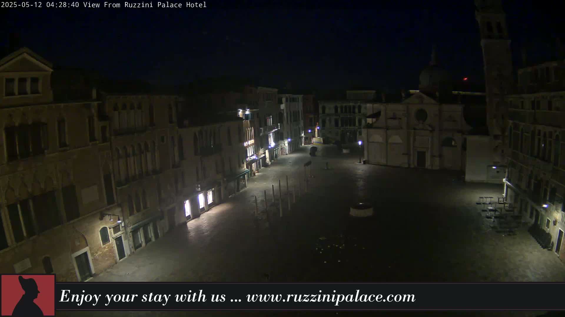 A nighttime, high-angle view of a deserted Venetian piazza, surrounded by old buildings, with a church in the background.