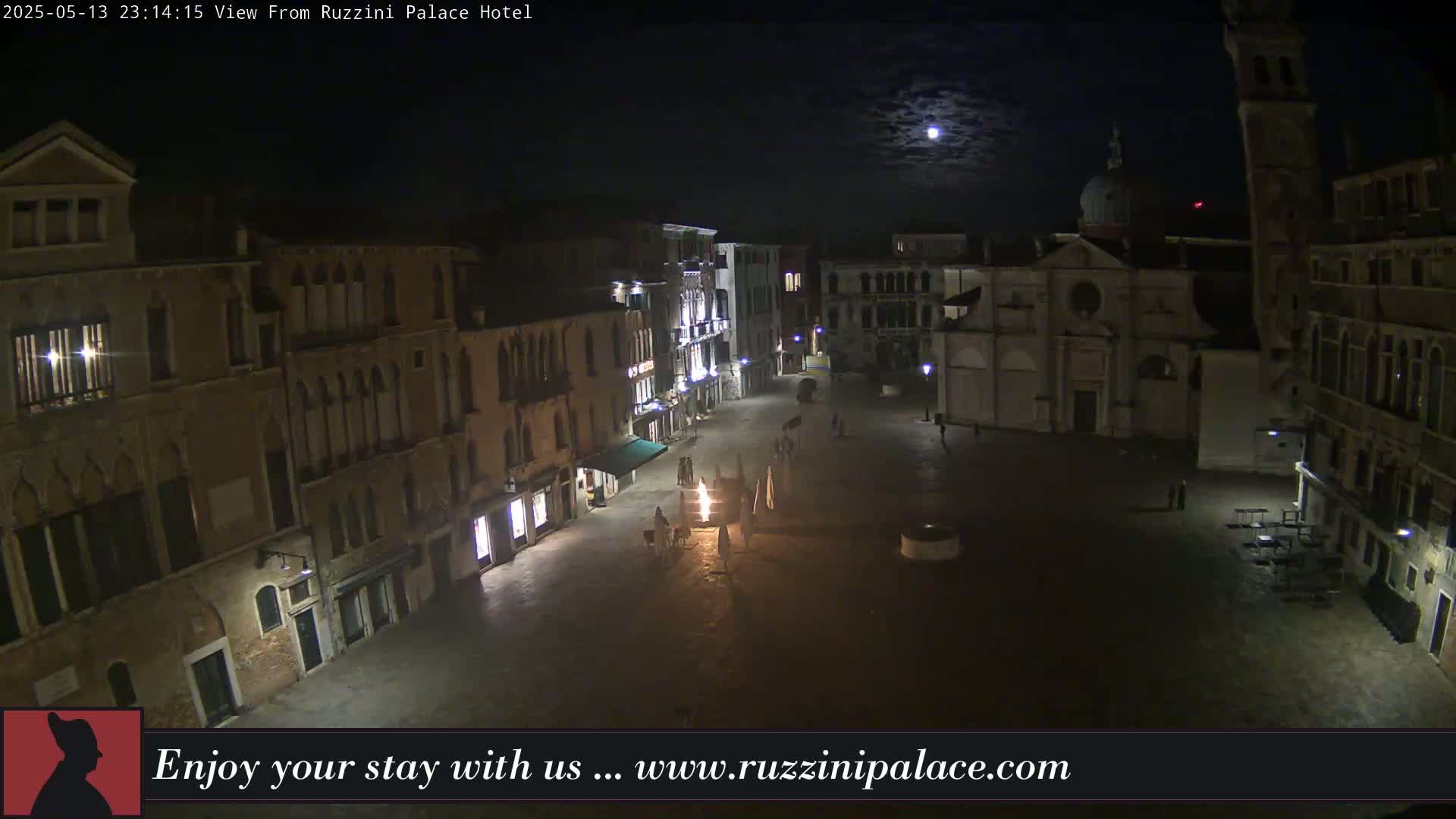 A moonlit, nighttime view of a mostly empty plaza in Venice, Italy, surrounded by old buildings.