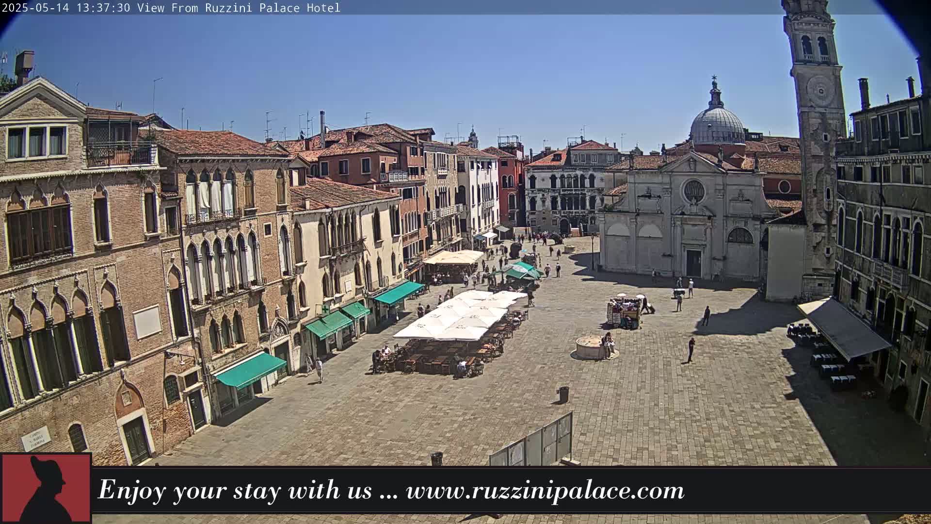 A sunny day reveals a large, paved square in Venice, Italy, surrounded by historic buildings with outdoor cafes.