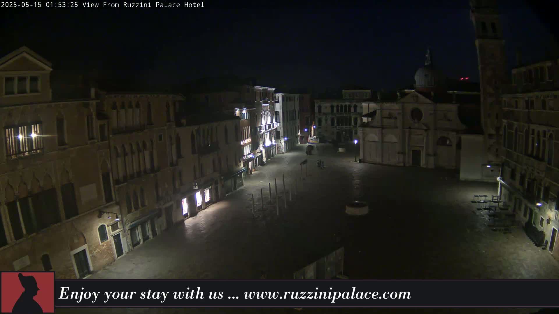 A nighttime, aerial view shows a mostly empty, dark plaza in Venice, Italy, surrounded by illuminated buildings.