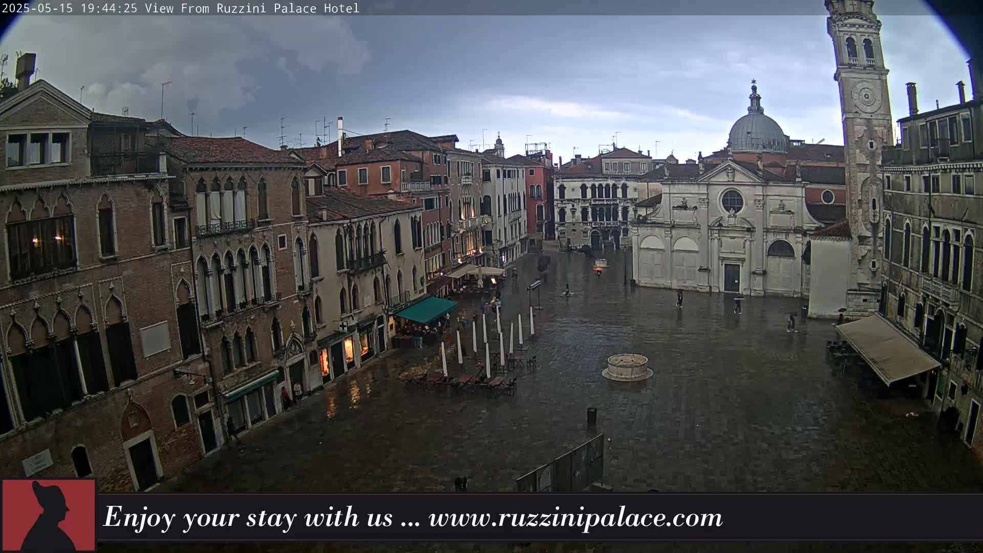 A rain-soaked Venetian square is surrounded by historic buildings, under a partly cloudy sky.