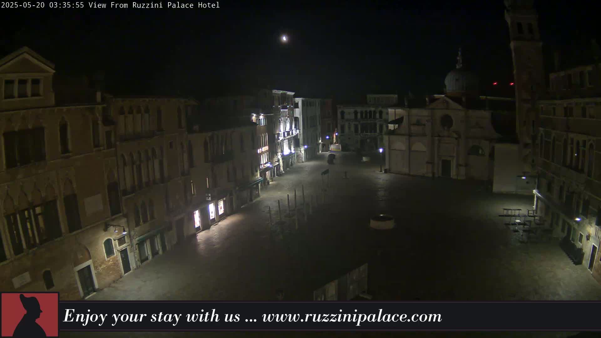 A nighttime view of a mostly empty, dimly lit square in Venice, surrounded by old buildings under a clear, moonlit sky.