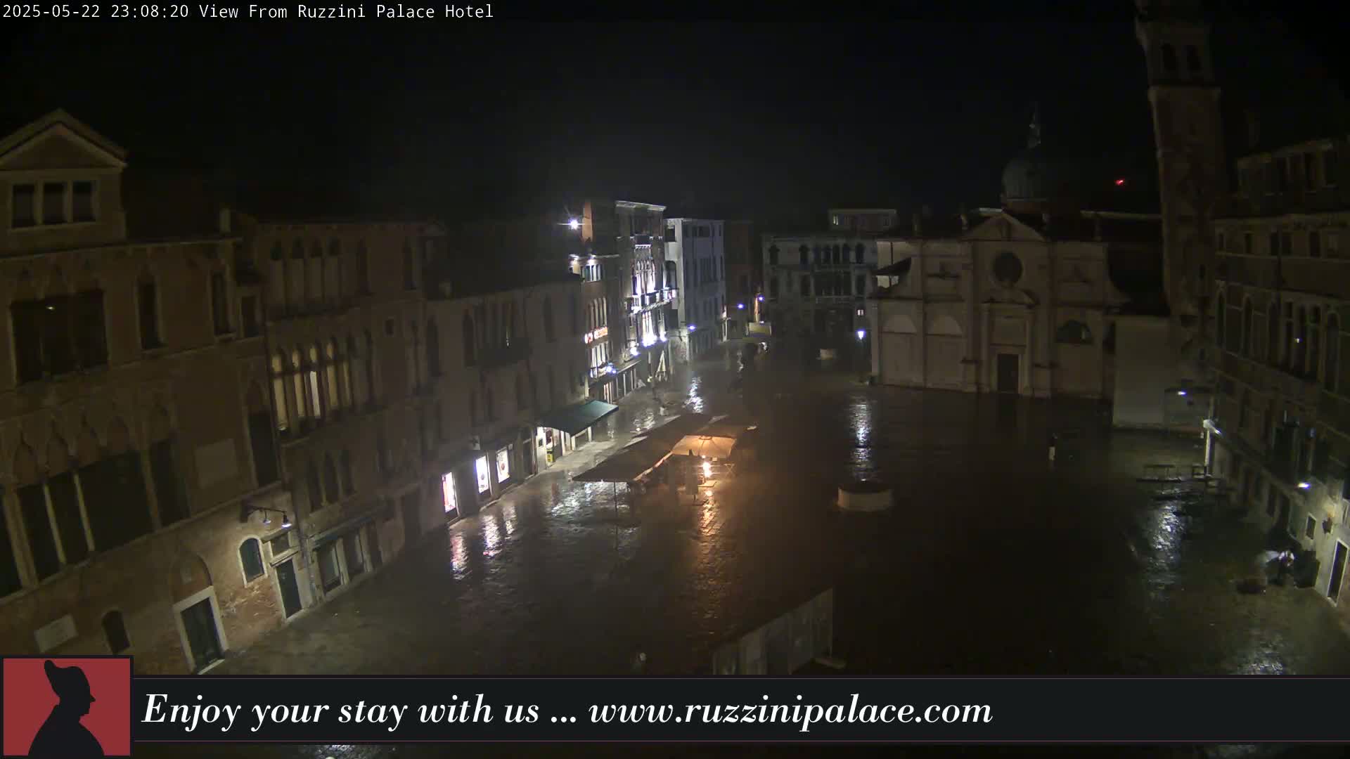 A nighttime view of a rain-soaked Venetian square, surrounded by historic buildings.