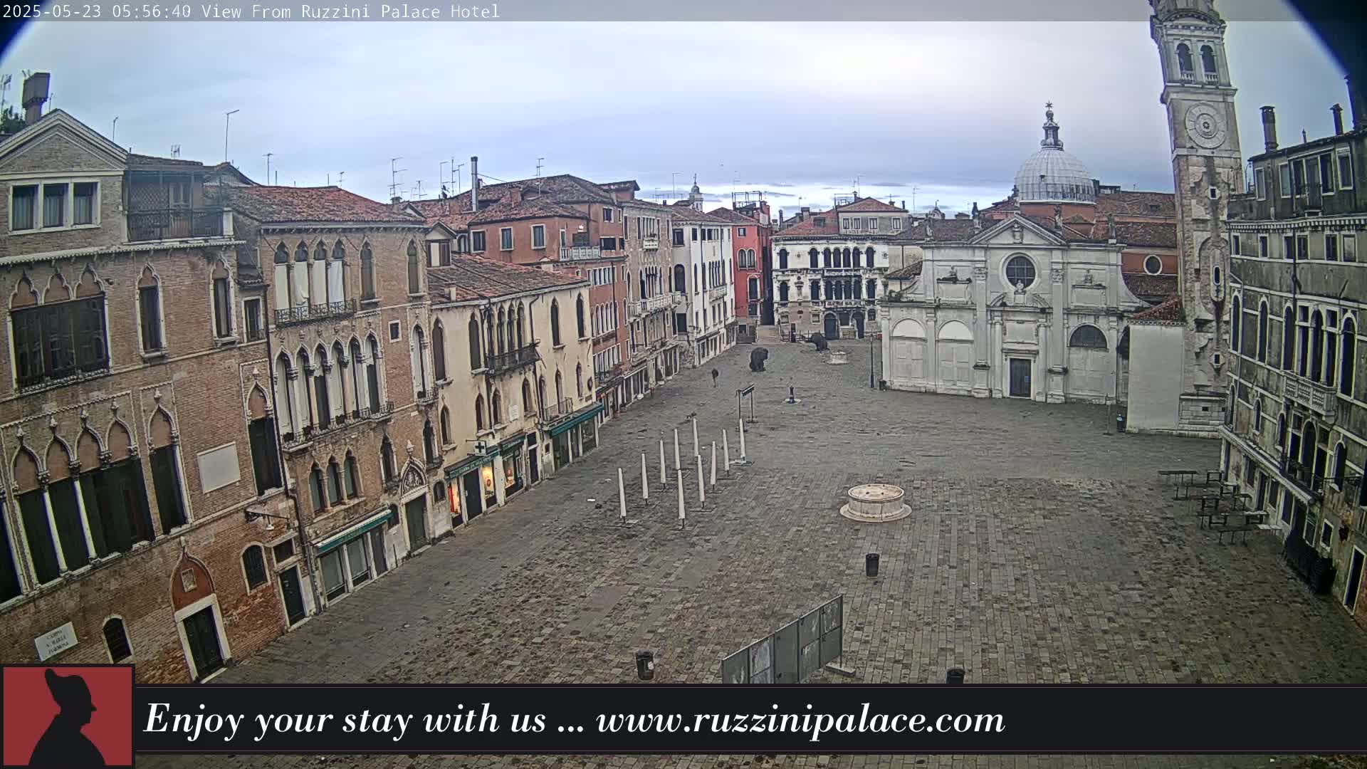 A mostly empty cobblestone square in Venice, Italy, is surrounded by old brick buildings under an overcast sky.