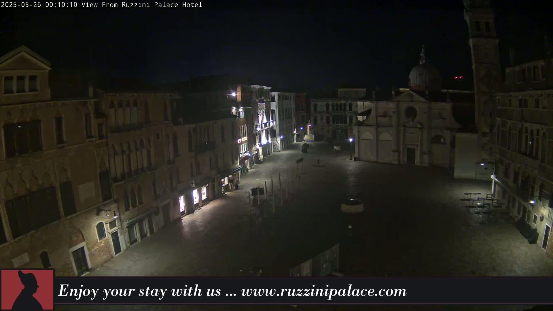 A nighttime view of a mostly empty, cobblestone square in Venice, surrounded by old buildings, with a church visible in the background.