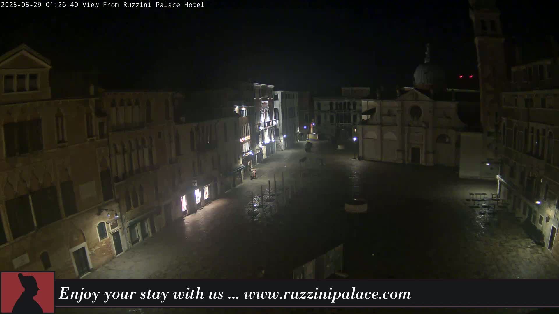 A nighttime, rain-slicked Venetian square is surrounded by old buildings under a dark sky.