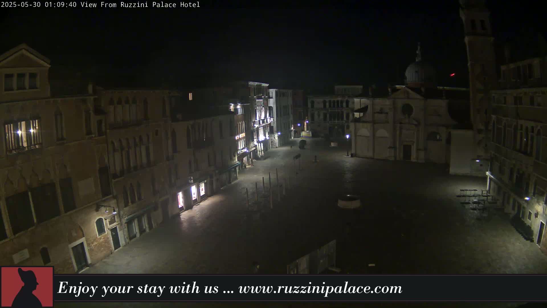 A nighttime, high-angle view of a dimly lit, empty plaza in Venice, Italy, surrounded by old buildings.