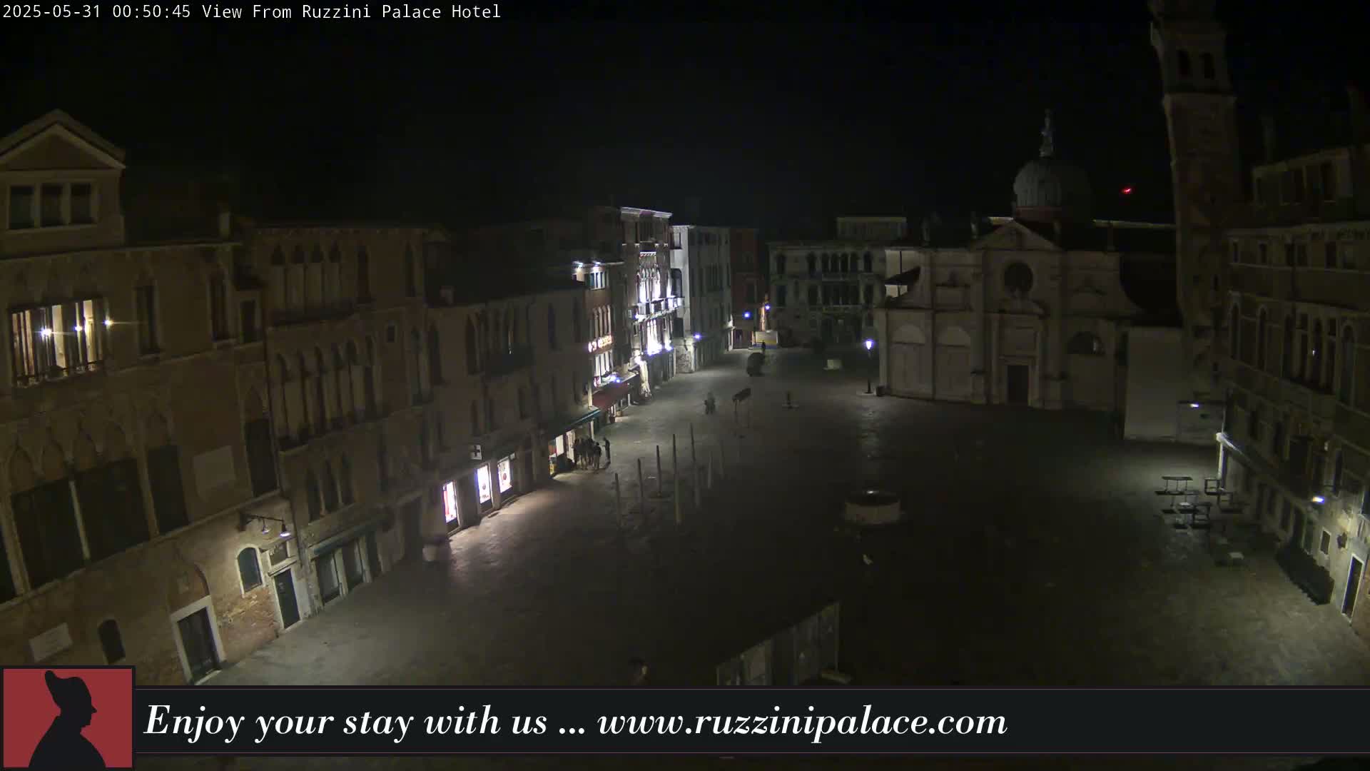 A nighttime, aerial view of a dimly lit, empty square in Venice, surrounded by tall buildings.