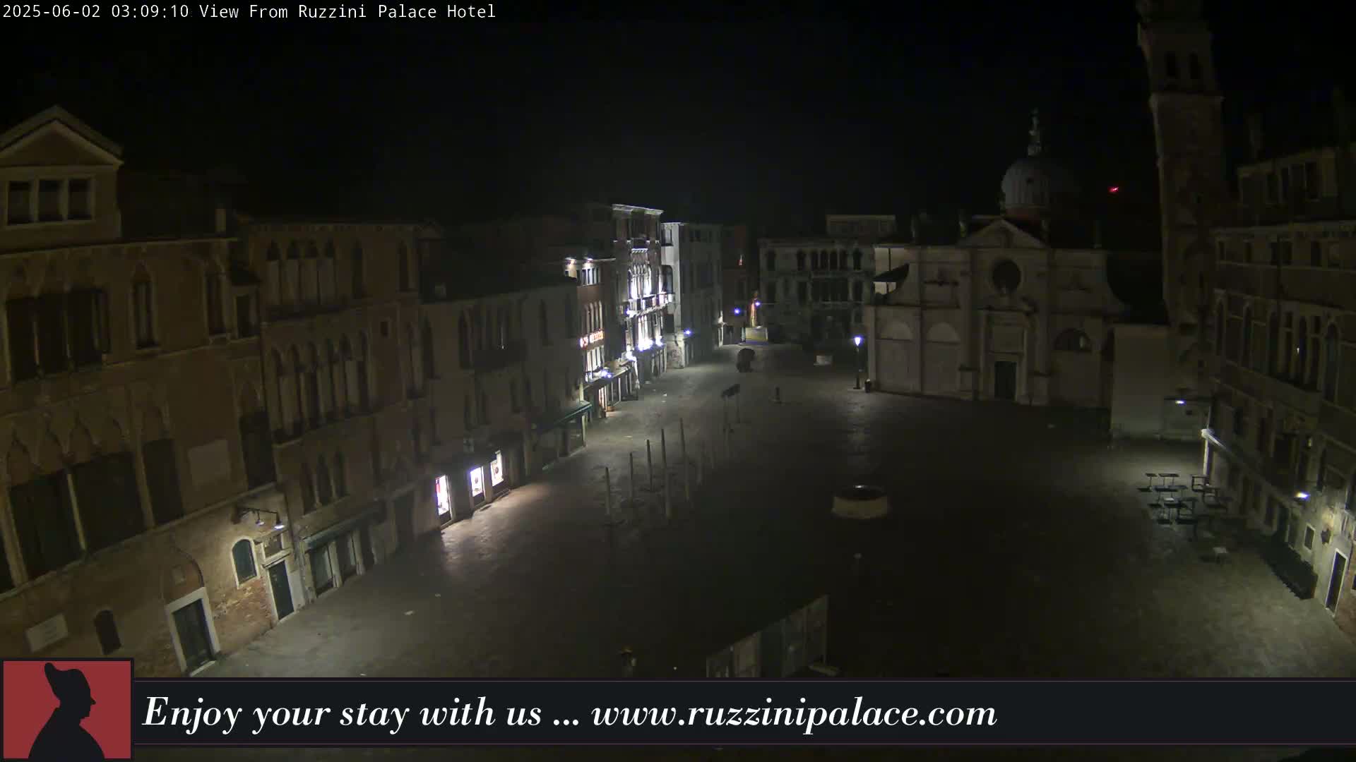 A nighttime, aerial view of a mostly empty European-style square, surrounded by old buildings.