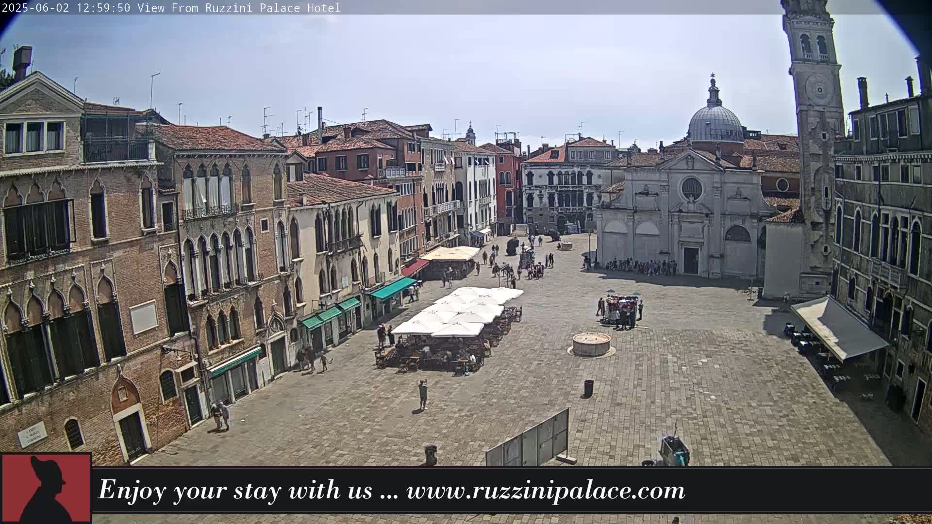 A sunny view of a large plaza in Venice, Italy, surrounded by historic buildings, with several people and outdoor seating areas visible.