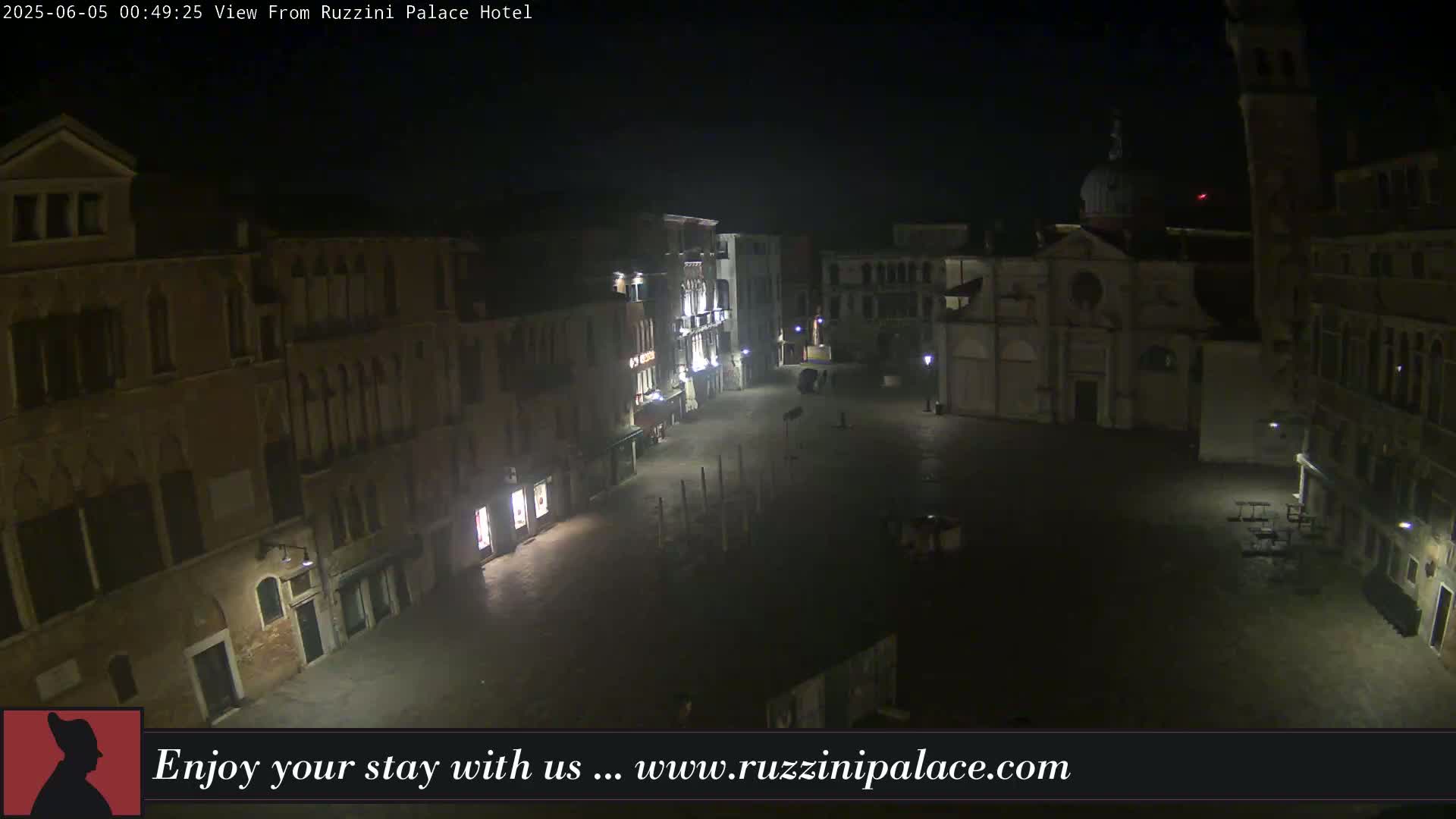 A nighttime view of a mostly empty plaza in a city, surrounded by old buildings under a dark sky.