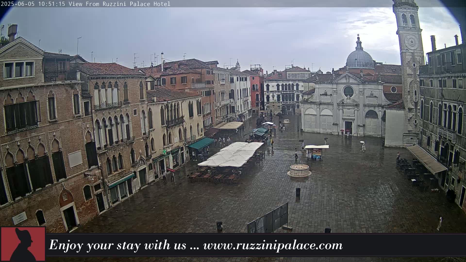A wet, stone plaza in Venice, Italy, is surrounded by historic buildings, some with arched windows, under an overcast sky.