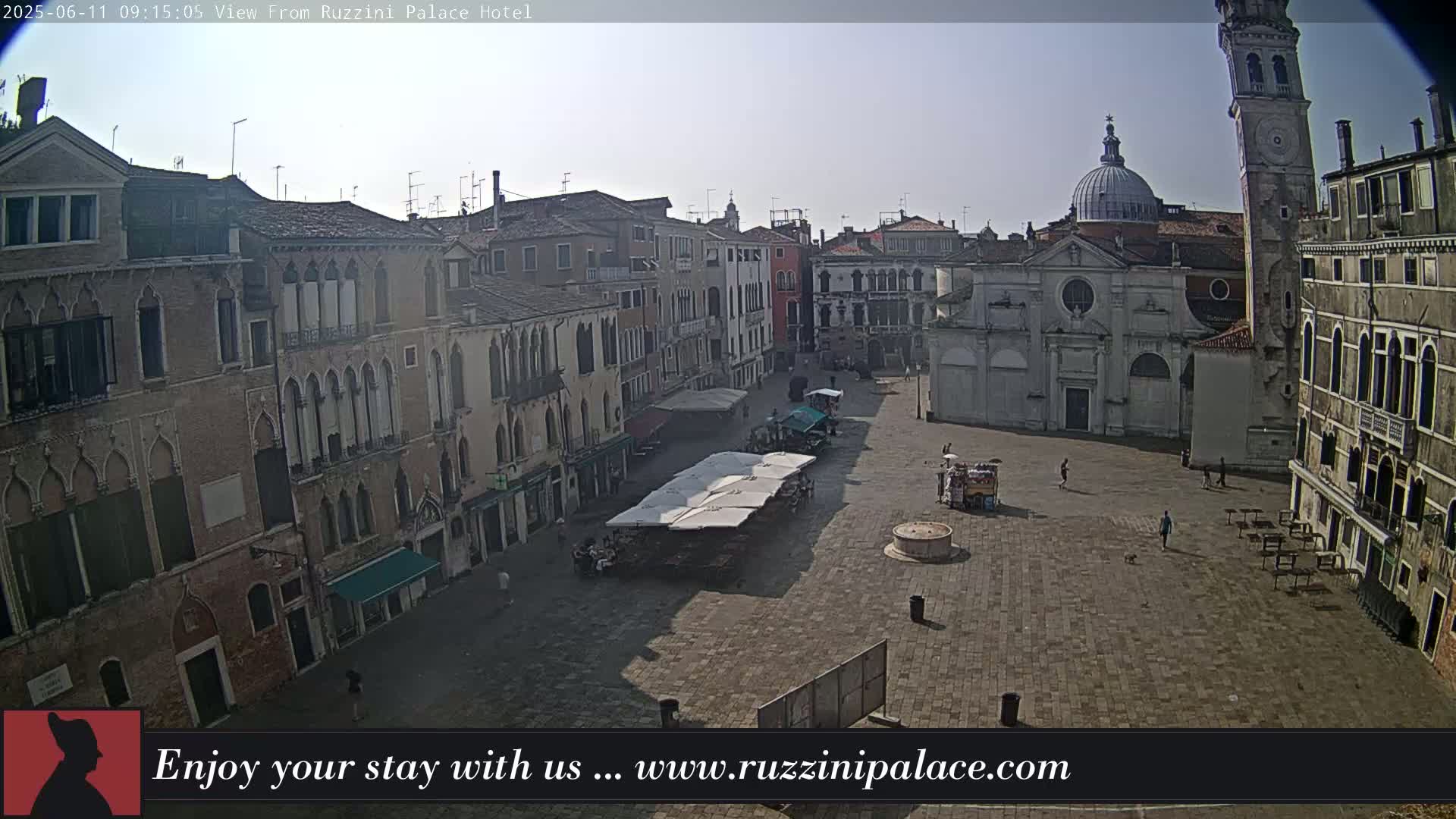 A mostly empty cobblestone square in Venice, Italy, is surrounded by old buildings under a bright, clear sky.