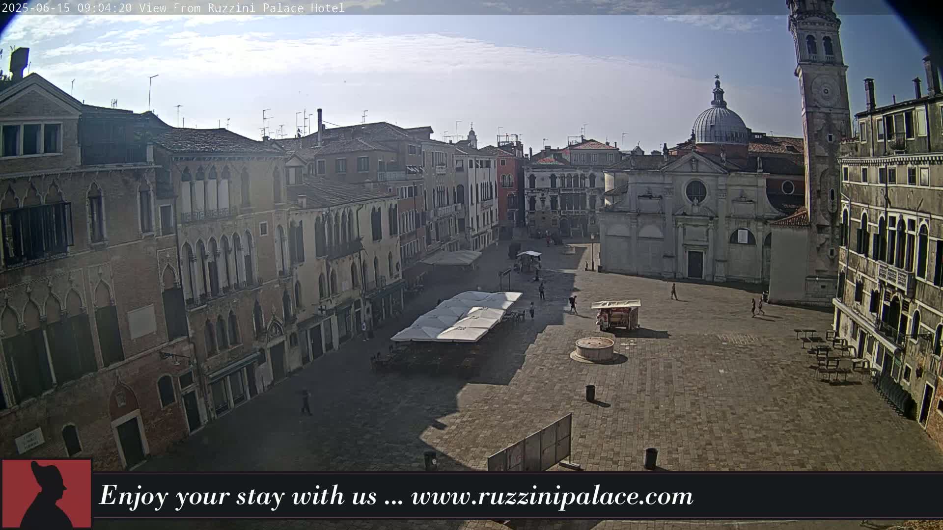 A mostly empty cobblestone square in Venice, Italy, is surrounded by tall buildings under a mostly clear sky.