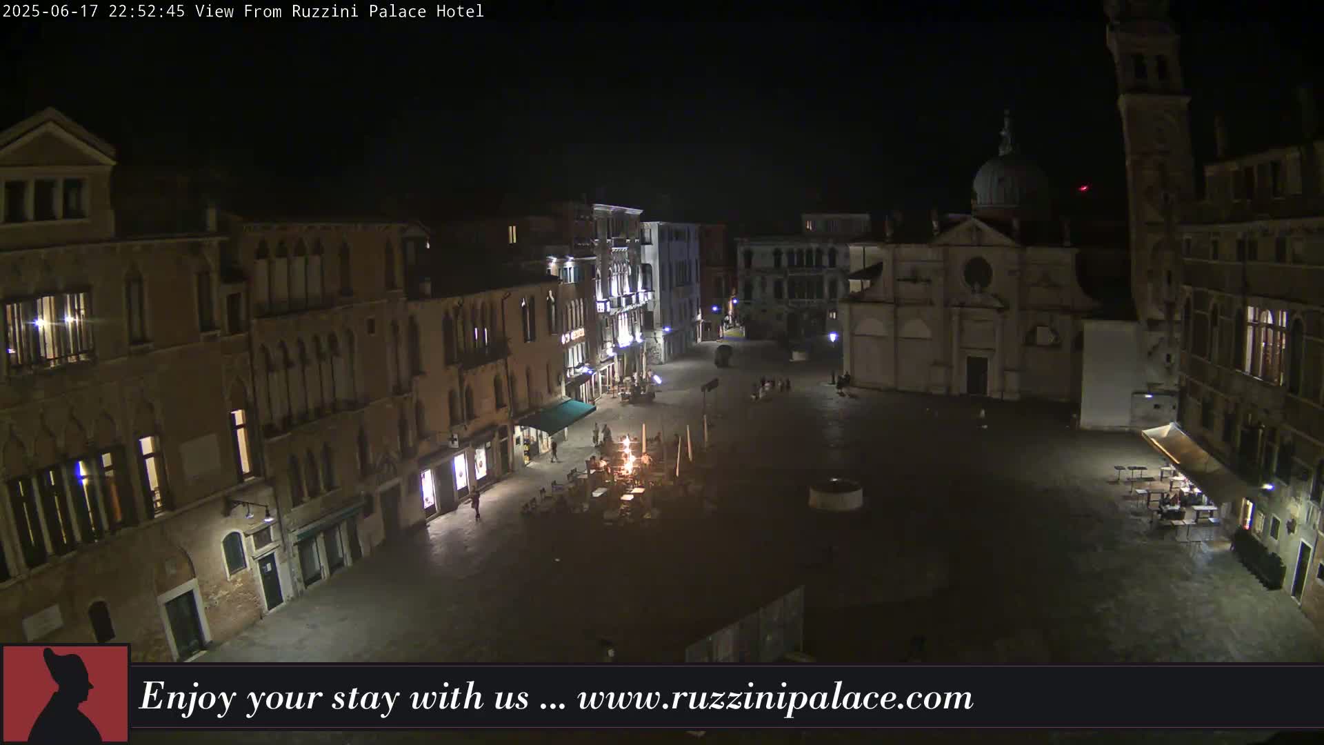 A nighttime, high-angle view of a dimly lit, cobblestone square in Venice, surrounded by historic buildings.