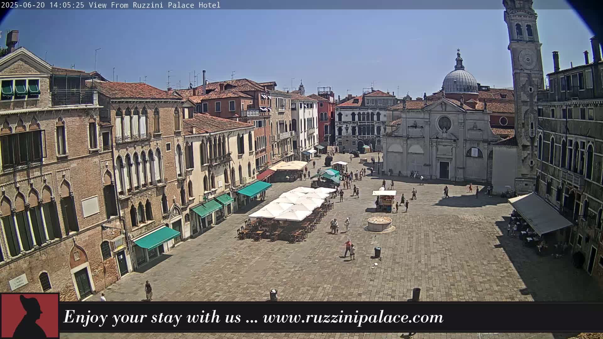 A sunny day reveals a large, paved square in Venice, Italy, surrounded by historic buildings, with several outdoor cafes and a few people scattered about.