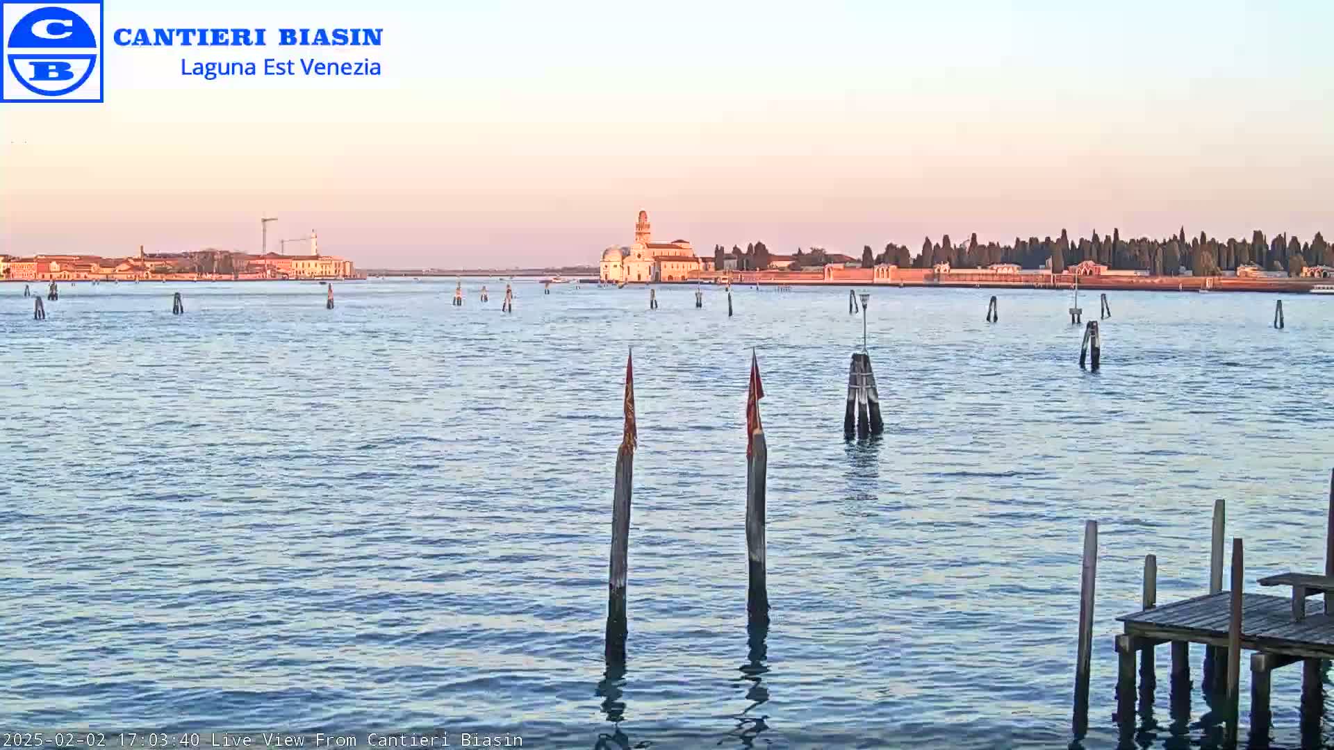 A calm body of water with a distant cityscape under a pale pink sky.