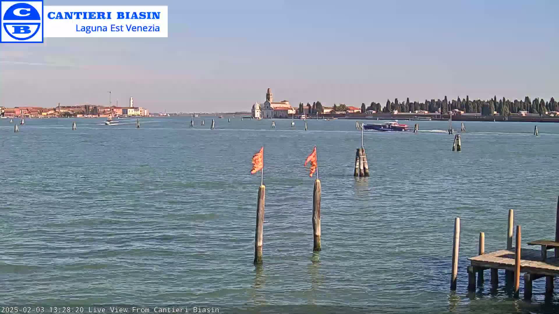 A calm, sunny day shows a body of water with boats and a distant island featuring buildings and trees.
