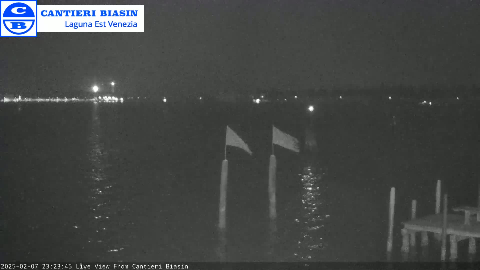 A nighttime view of a calm body of water with two flags on posts and a small dock in the lower right corner.