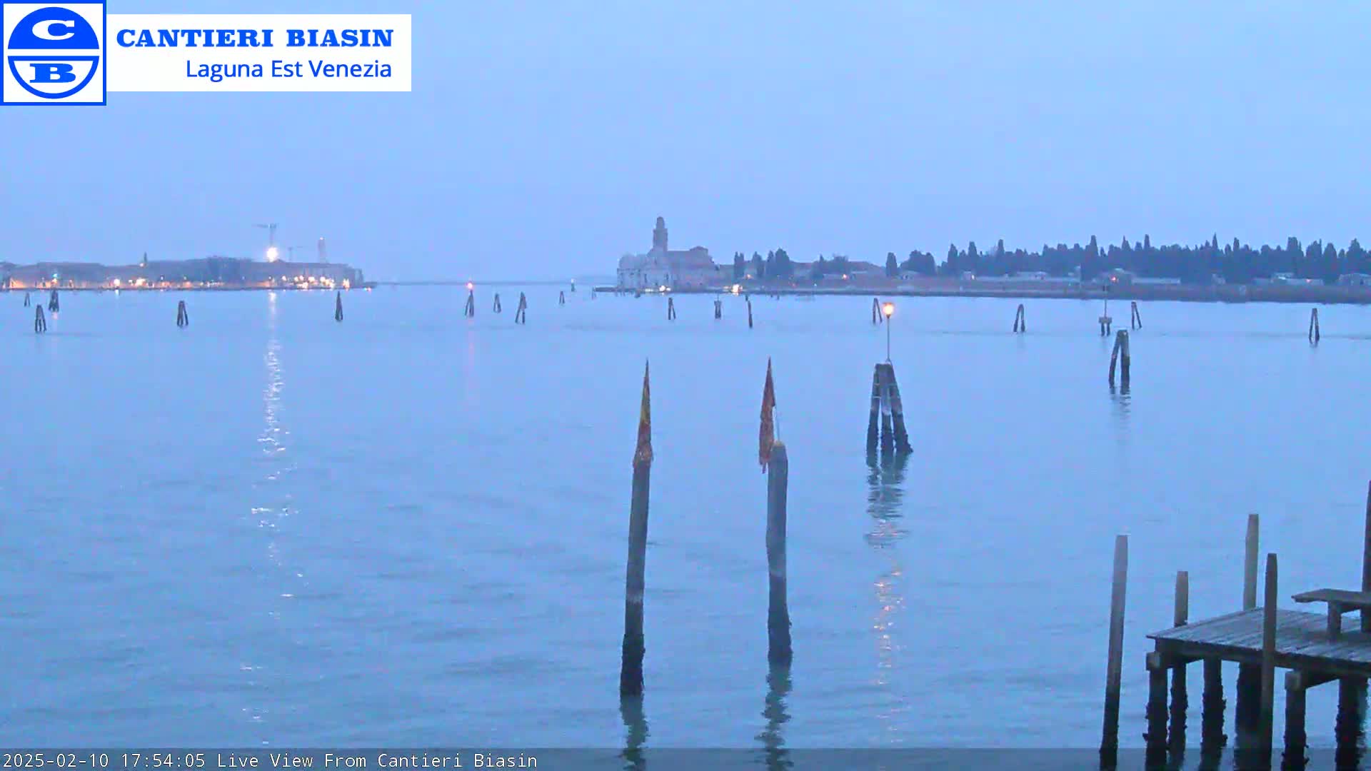 A calm, twilight view of a waterway with numerous wooden posts and a distant building on a shoreline.